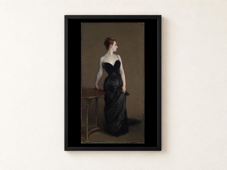 May include: A framed art print of a painting depicting a person with reddish-brown hair in an updo, wearing a floor-length black strapless gown with thin straps. The person stands beside a small wooden table against a muted brown background.