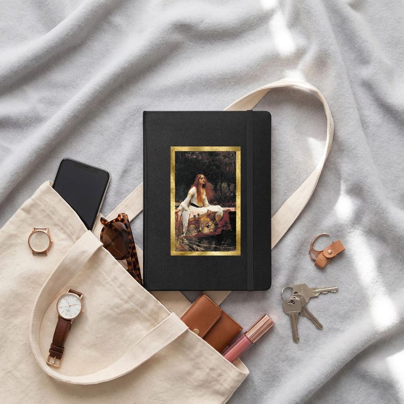 May include: A black hardcover notebook featuring a rectangular print of John William Waterhouse's The Lady of Shalott with a gold border. The notebook is placed inside a beige canvas tote bag alongside a smartphone, sunglasses, a watch, keys, and a small wallet.