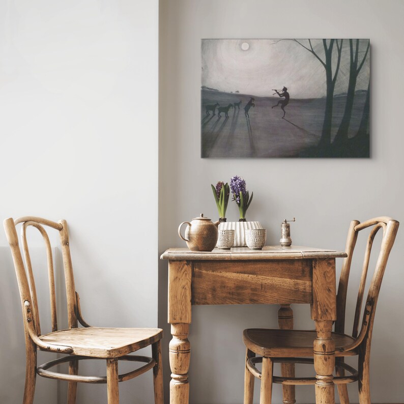 May include: A rectangular wall art print depicts a silhouetted figure playing a flute for animals in a misty landscape. Below, a wooden table holds a brown teapot, two small cups, a white vase with purple hyacinths, and a metal grinder.