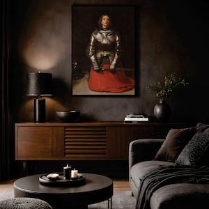 May include: A framed wall art print depicting a figure in polished silver plate armor with a vibrant red skirt, holding a sword. The artwork is displayed above a dark wooden sideboard in a room with a black lamp, a bowl, and books.