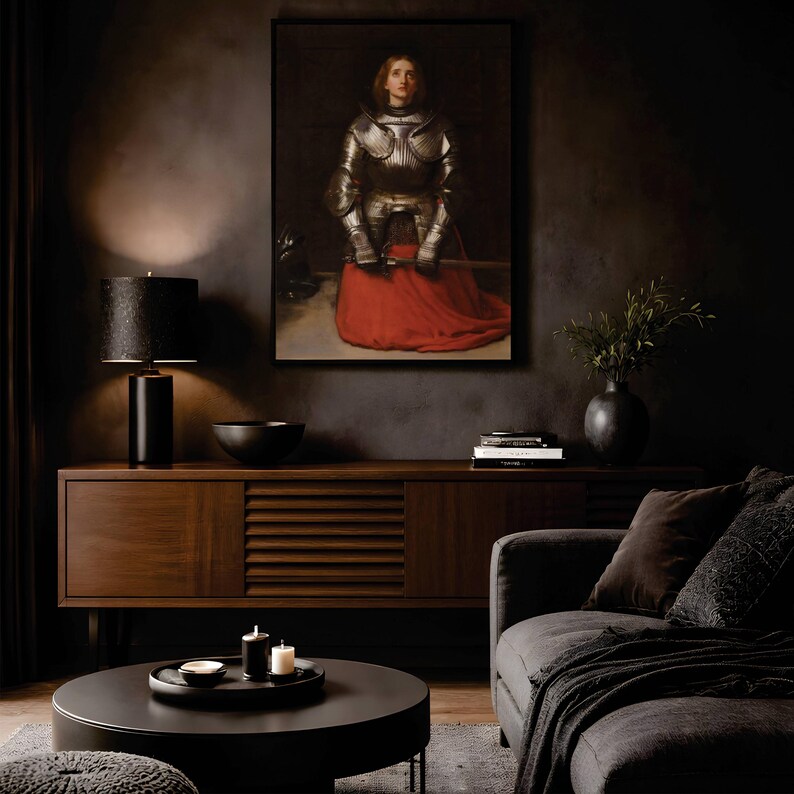 May include: A framed wall art print depicting a figure in polished silver plate armor with a vibrant red skirt, holding a sword. The artwork is displayed above a dark wooden sideboard in a room with a black lamp, a bowl, and books.