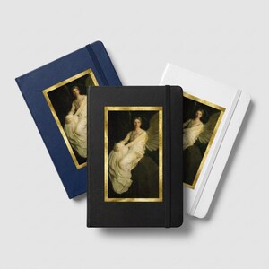 May include: Three hardcover journals in navy blue, black, and white, each featuring a vertical rectangular inset print of a seated winged figure in a white gown, framed by a gold border. Each notebook includes a matching elastic closure band.