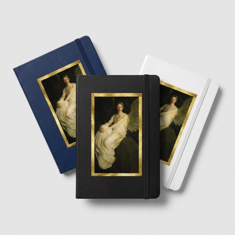 May include: Three hardcover journals in navy blue, black, and white, each featuring a vertical rectangular inset print of a seated winged figure in a white gown, framed by a gold border. Each notebook includes a matching elastic closure band.