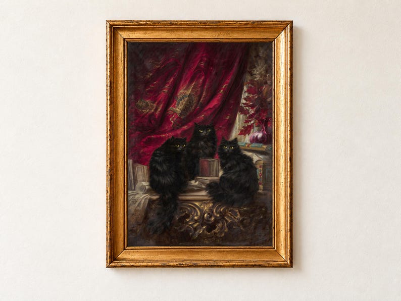 Three Black Cats by Carl Kahler as a framed print in an antique gold frame on a cream wall. Three long-haired black cats with amber eyes sit together in front of a draped crimson curtain.