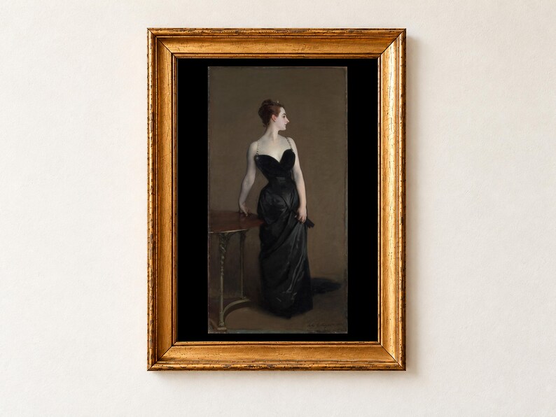 Madame X by John Singer Sargent, 1884, as a framed print in an antique gold frame on a cream wall. A woman in a black satin evening gown with jewelled straps stands in profile, one hand resting on a small round table, against a warm brown background, shown with a black border.