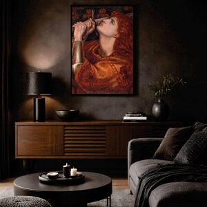 May include: A framed rectangular wall art print featuring a painting of a person with long red hair, wearing a metallic arm guard and holding a sword near their face. The artwork displays warm orange and brown tones with dark accents.