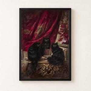 Three Black Cats by Carl Kahler as a framed print in a black frame on a cream wall. Three long-haired black cats with yellow eyes sit on a gilded table among books and scrolls, in front of a crimson velvet curtain embroidered in gold.
