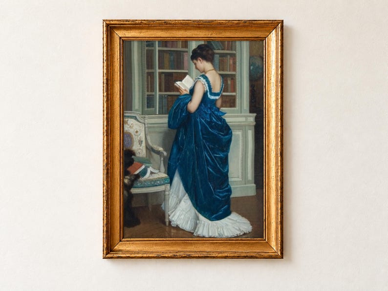 In the Library by Auguste Toulmouche, 1872, as a framed print in an antique gold frame on a cream wall. A young woman in a blue silk gown with a white ruffled train stands reading a small book before tall glass-fronted bookcases.