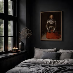 May include: A framed wall art print depicting a person in metallic plate armor and a long red skirt, displayed in a bedroom with gray bedding, a black vase with dried branches, and two lit candles on a windowsill near a window.