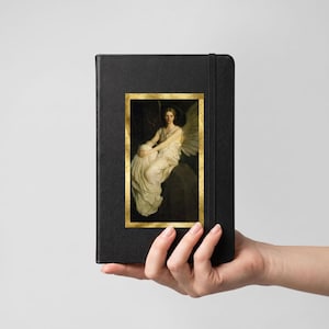 May include: A black hardcover notebook featuring a rectangular print on the front cover. The print displays a painting of a winged figure in a white gown sitting on a stone ledge, framed by a gold border. An elastic band secures the notebook closed.
