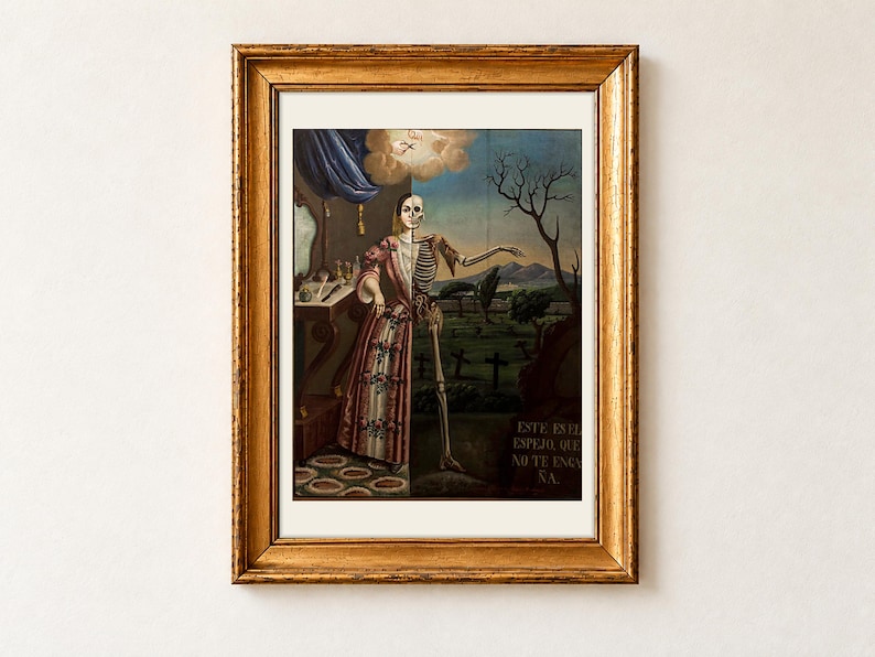 Allegory of Death by Tomas Mondragon, 1856, as a framed print with a cream border in an antique gold frame on a cream wall. A woman in a rose-patterned gown stands by her dressing table, the right half of her body a skeleton, beside a graveyard and the painted words Este es el espejo que no te engana.