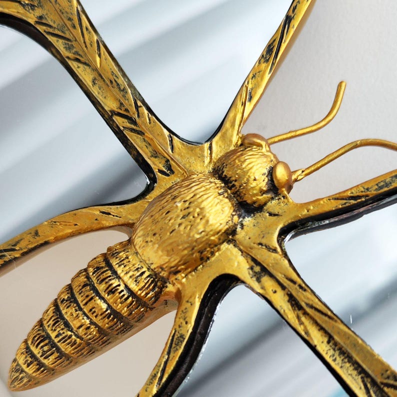 May include: A close-up of a decorative butterfly mirror. The butterfly is gold with black accents, and the wings are outstretched. The mirror has a detailed, textured design, and the overall aesthetic is vintage.