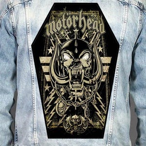 May include: A light blue denim jacket featuring a large, coffin-shaped back patch with a black and gold graphic. The design displays the text "motörhead" above a horned skull, chains, lightning bolts, and stars on a dark, textured background.