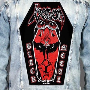 May include: A light blue denim jacket featuring a large, coffin-shaped back patch. The patch displays a red and black graphic of a face with a pentagram on the forehead, a snake, the text Venom at the top, and Black Metal on the sides.