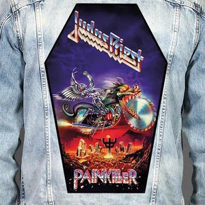 May include: A light blue denim jacket featuring a large, coffin-shaped back patch. The patch displays the Judas Priest logo and the word PAINKILLER, with a graphic of a metallic, winged figure riding a motorcycle with a circular saw blade wheel.