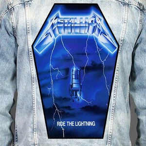 Op de afbeelding: Een lichtblauw spijkerjack met een grote, doodskistvormige patch op de rug. De patch toont het Metallica-logo in metallic blauw, een afbeelding van een elektrische stoel, witte bliksemschichten tegen een donkerblauwe achtergrond en de tekst RIDE THE LIGHTNING.