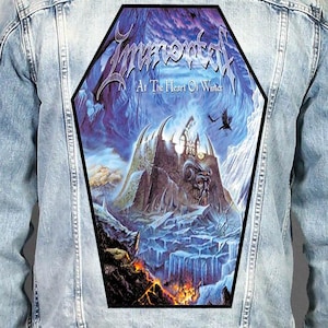 Könnte beinhalten: Eine hellblaue Jeansjacke mit einem großen, sargförmigen Rückenaufnäher. Der Aufnäher zeigt eine Fantasielandschaft mit einer Steinfestung, eisigen Bergen, einem Raben und Lava sowie dem aufgedruckten Text Immortal und At The Heart Of Winter.