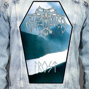 May include: A light blue denim jacket featuring a large, coffin-shaped patch on the back. The patch displays a landscape of mountains and a river with stylised, metallic-coloured text at the top and the word FROST in light blue lettering below.