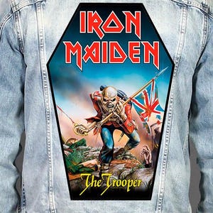May include: A light blue denim jacket featuring a large, coffin-shaped back patch. The patch displays the Iron Maiden logo, the text The Trooper, and a graphic of a skeletal soldier in a red uniform holding a sword and a tattered British flag.