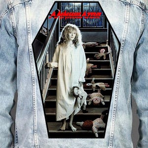 May include: A light blue denim jacket featuring a large coffin-shaped back patch. The patch displays a person in a white nightgown standing on stairs surrounded by several dolls, with the red text ANNIHILATOR printed at the top of the graphic.