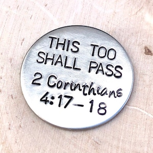 May include: A silver-toned round token with the text "This Too Shall Pass 2 Corinthians 4:17-18" engraved on it.