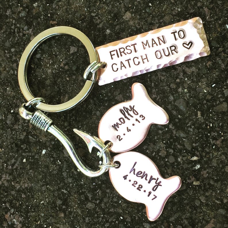 May include: A silver key chain with a hook and two copper fish charms. The fish charms are engraved with the names "Molly" and "Henry" and their birth dates. The key chain also has a copper tag that reads "First Man To Catch Our &hearts;".