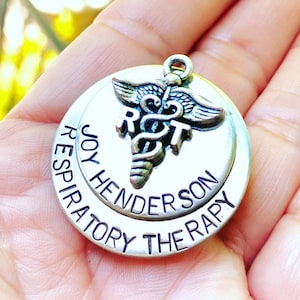 May include: Silver charm with a medical symbol and the text "JOY HENDERSON RESPIRATORY THERAPY".
