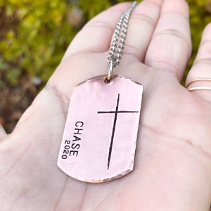 May include: A copper dog tag necklace with a cross and the text "CHASE 2020" engraved on it.