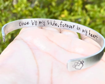 May include: Silver bracelet with the inscription "Once by my side, forever in my heart" and a paw print with a heart inside.