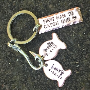 May include: A silver key chain with a hook and two copper fish charms. The fish charms are engraved with the names "Molly" and "Henry" and their respective dates. The key chain also has a copper tag that reads "First Man To Catch Our &hearts;".