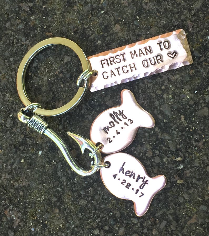May include: A silver key chain with a hook and two copper fish charms. The fish charms are engraved with the names "Molly" and "Henry" and their respective dates. The key chain also has a copper tag that reads "First Man To Catch Our &hearts;".