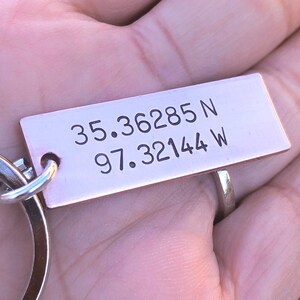 May include: A copper keychain with a silver ring. The keychain has the coordinates "35.36285 N 97.32144 W" engraved on it.