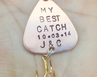 Op de afbeelding: Een koperkleurige vislokaas met de tekst "My Best Catch 10.03.14 J&C" erop gegraveerd. Het lokaas heeft een gouden haak.