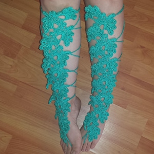 Puede incluir: Envolturas de piernas de ganchillo turquesa con diseños florales. Las envolturas se extienden desde los pies hasta las piernas, aseguradas con lazos de cuerda. Las envolturas hechas a mano son un accesorio único.
