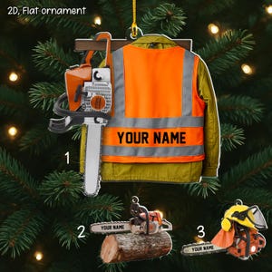 May include: A flat Christmas ornament featuring a chainsaw, a safety vest with "YOUR NAME" printed on it, and a chainsaw on a log. The ornament is orange, silver, and yellow. The text "2D, Flat ornament" is at the top.
