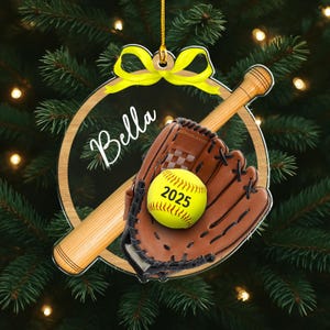 Pode incluir: Enfeite de Natal com tema de softball. Apresenta uma bola de softball amarela com o ano de 2025, uma luva marrom e um bast&atilde;o de madeira. O enfeite inclui o nome "Bella" e um la&ccedil;o amarelo.