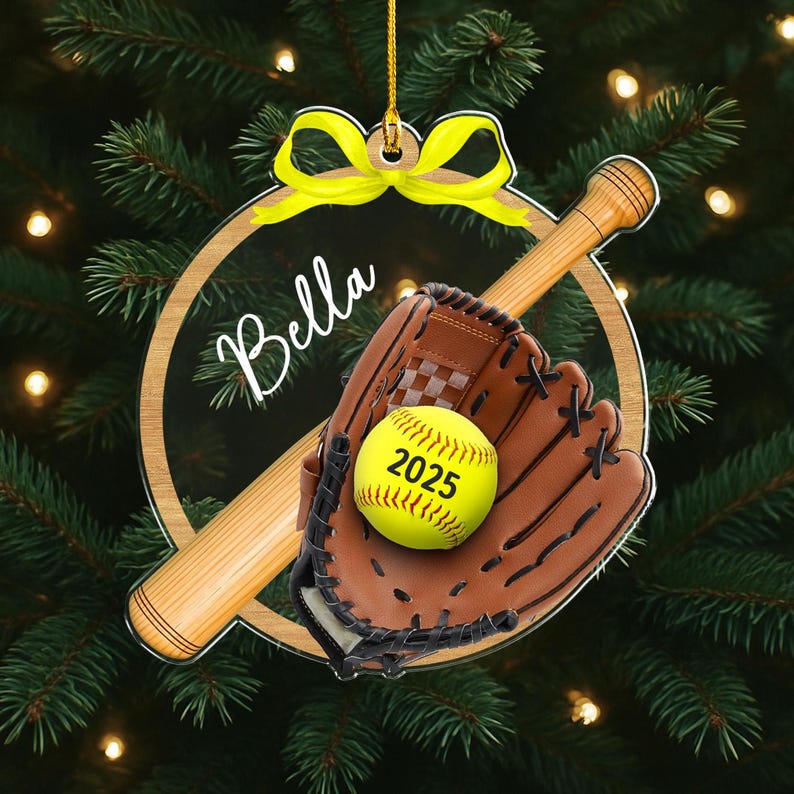 Pode incluir: Enfeite de Natal com tema de softball. Apresenta uma bola de softball amarela com o ano de 2025, uma luva marrom e um bast&atilde;o de madeira. O enfeite inclui o nome "Bella" e um la&ccedil;o amarelo.