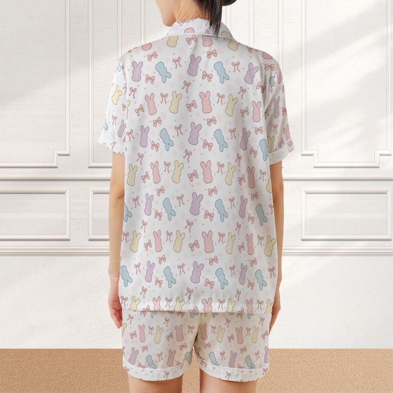 May include: White pajama set with a pastel bunny and bow pattern. The short-sleeved top and shorts feature a repeating design of bunnies in blue, yellow, pink, and purple, along with matching bows. The sleepwear set is made of a soft, lightweight fabric.