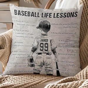 Puede incluir: Un cojín decorativo con temática de béisbol con el texto "BASEBALL LIFE LESSONS" y un gráfico de un jugador de béisbol. La camiseta del jugador muestra el nombre "JAMES" y el número "99". El cojín también presenta citas inspiradoras.