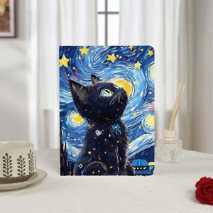 Könnte beinhalten: Ein Notizbuch mit einer schwarzen Katze, die in einen wirbelnden Nachthimmel mit gelben Sternen und einem großen gelben Mond blickt. Das Design erinnert an Van Goghs "Sternennacht". Die Katze hat ein weißes Herz- und Stern-Design.