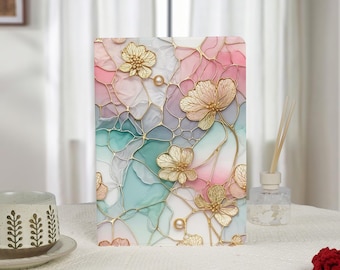 Puede incluir: Panel rectangular decorativo con diseño floral. El panel presenta flores doradas y detalles de perlas sobre un fondo de formas abstractas rosas, azules y blancas. El panel está sobre una superficie blanca.