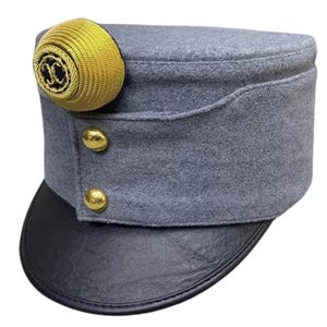 May include: A grey military-style hat with a black leather peak. It has a gold-coloured decorative emblem and two gold buttons. This hat is likely a historical or costume item.