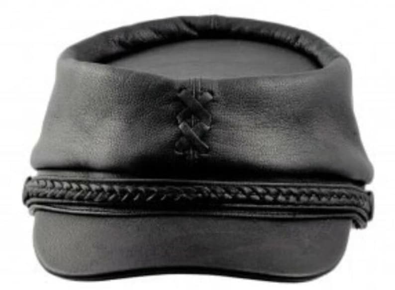 May include: Black leather hat with a rounded crown and a braided band around the base. The hat features a decorative cross-stitch detail on the front. The hat is a dark, solid color.