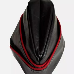Può includere: Un cappello nero in stile militare con finiture rosse. Il cappello è realizzato in un materiale liscio, forse simile alla pelle. La finitura rossa è una sottile corda decorativa che borda i bordi del cappello.