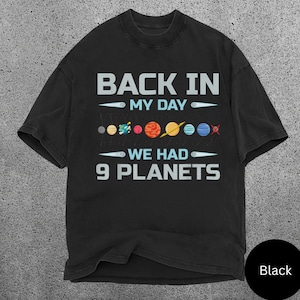 May include: Black t-shirt featuring the text "BACK IN MY DAY WE HAD 9 PLANETS" in light blue, with illustrations of planets. The shirt has a crew neck and short sleeves.