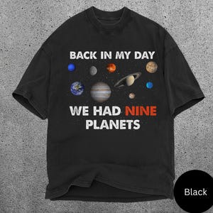 May include: Black t-shirt with a graphic of planets and the text "BACK IN MY DAY WE HAD NINE PLANETS". The planets are in various colours, including blue, orange, and brown. The text is in white and red.