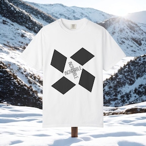 Peut inclure: T-shirt blanc avec un motif géométrique noir et le mot "INCREDIBLE" en blanc. Le t-shirt est présenté sur un fond de montagnes enneigées, avec le soleil brillant en arrière-plan.