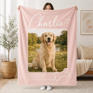 May include: A soft, light pink fleece blanket featuring a large, centered photograph of a golden retriever sitting in a grassy field. The name Charlie is printed in white script above the photo, with a white bone icon and memorial text below.
