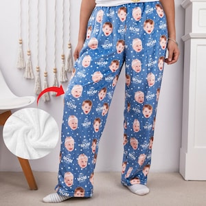 Puede incluir: Pantalones de pijama azules con un patrón repetido de caras de bebé y el texto "BEST MOM EVER". Los pantalones están hechos de un material suave y afelpado. Los pantalones de pijama son una opción de ropa de dormir cómoda.