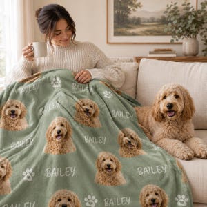 May include: A sage green fleece blanket featuring a repeating pattern of a golden doodle dog's face, white paw prints, and the name Bailey in a white script font. The soft fabric displays multiple portraits of the same curly-haired dog.